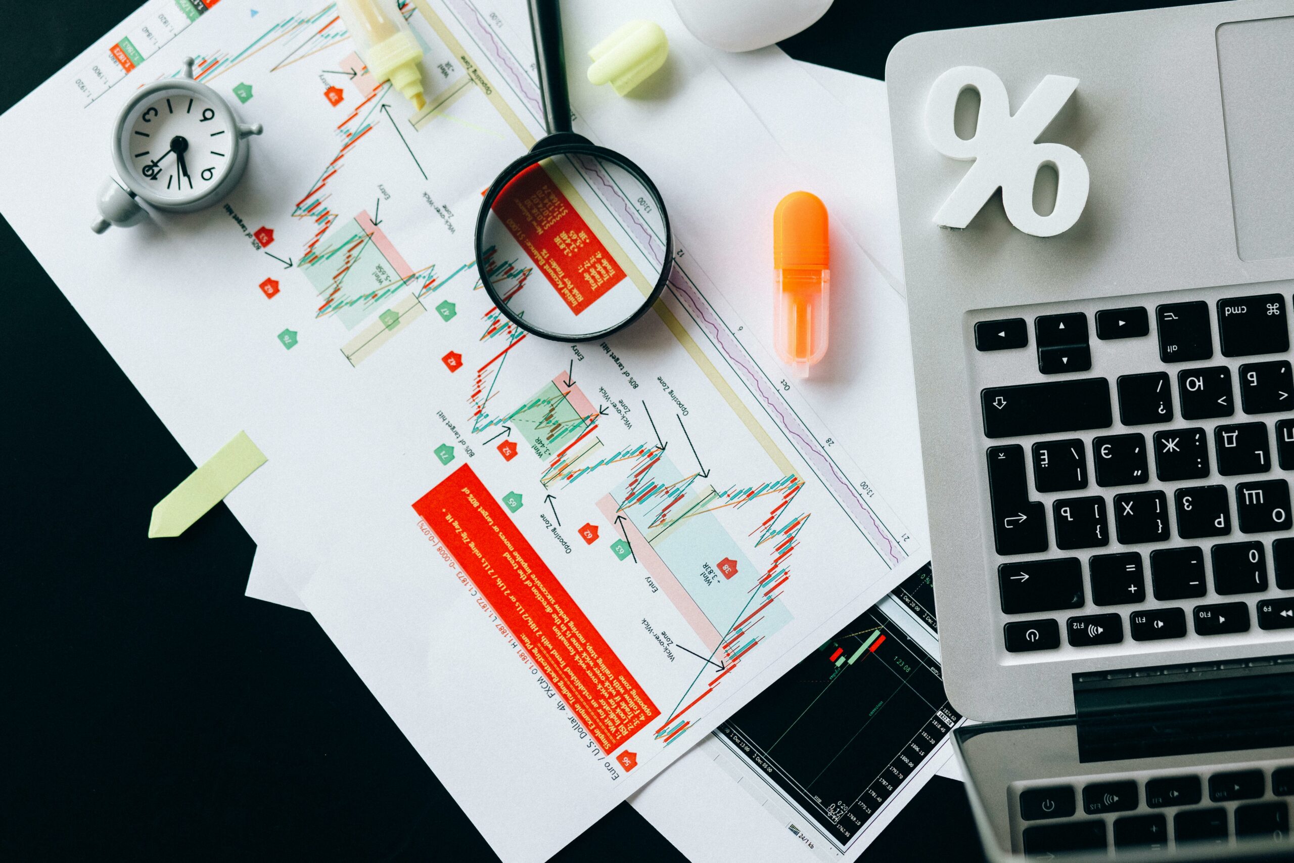 Top view of a desk with a laptop, percentage symbol, graphs, and magnifying glass used as a visualization of the numbers and data needed for SR&ED tax incentive program Image retrieved from pexels-nataliya-vaitkevich-6120214