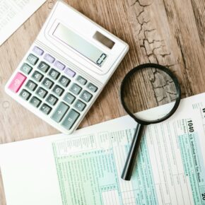 A top view of a wooden desk that has a magnifying glass, calculator and Canadian tax forms on top of a table, used for SR&ED Tax Consultant The InGenuity Group SR&ED Education and Resources. Image by RDNE Stock project: https://www.pexels.com/photo/a-calculator-and-a-magnifying-glass-beside-documents-7821688/