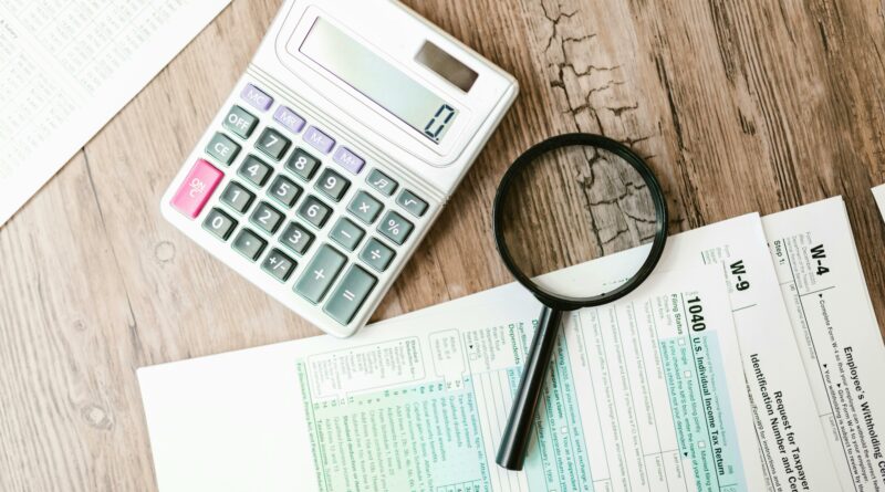 A top view of a wooden desk that has a magnifying glass, calculator and Canadian tax forms on top of a table, used for SR&ED Tax Consultant The InGenuity Group SR&ED Education and Resources. Image by RDNE Stock project: https://www.pexels.com/photo/a-calculator-and-a-magnifying-glass-beside-documents-7821688/